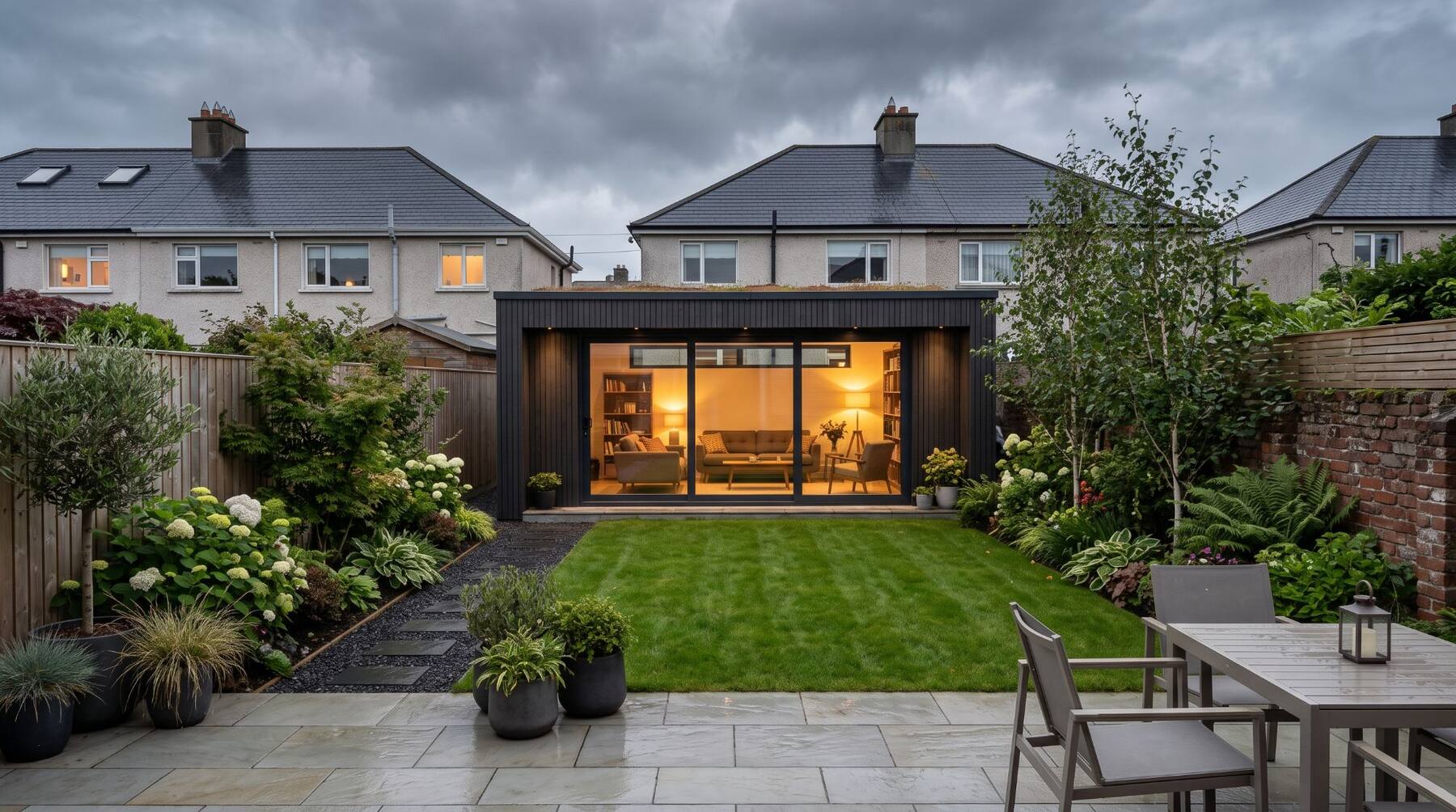 A modern garden room lit up at dusk at the end of an Irish back garden